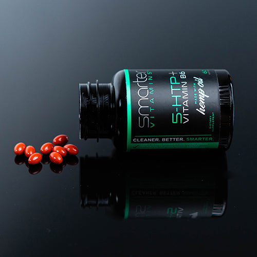 Bottle of Smarter 5-HTP laying on a black reflective table with supplements spilled out.